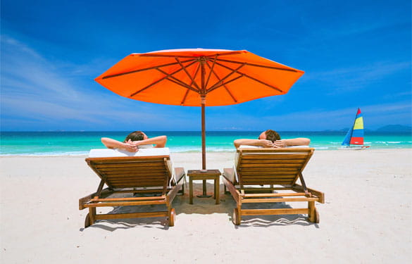 Couple on a tropical beach relax in the sun on deck chairs under a red umbrella travel