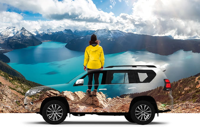 Woman in yellow jacket, overlooking lake at mountains. Car rental transparent overlay in foreground.