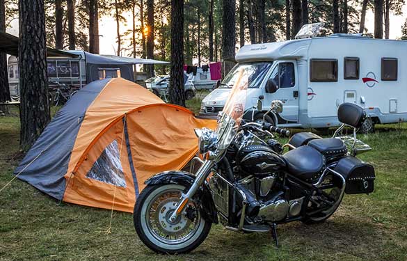 Black motorcycle parked next to an orange tent at a campground.